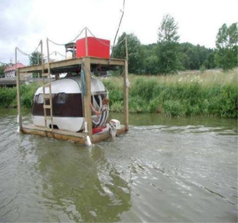 1989 Ford Bronco - A person steers a camper trailer converted into a boat, complete with an outboard motor and a wooden platform, elevated platform.