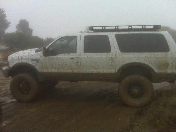 White lifted Ford Excursion SUV covered in mud on a foggy dirt trail