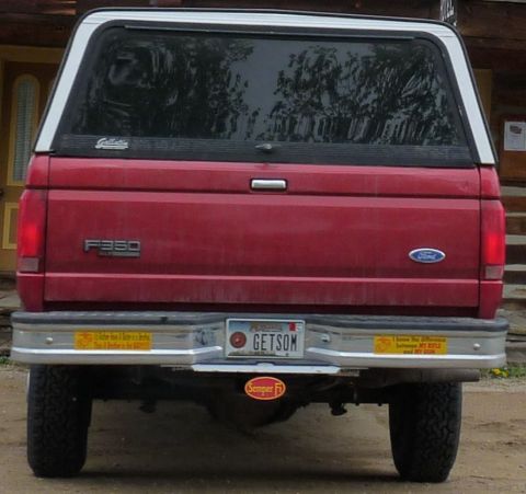 2006 Ford E350 - Rear view of a red Ford F350 pickup truck with a white camper shell and various bumper stickers.