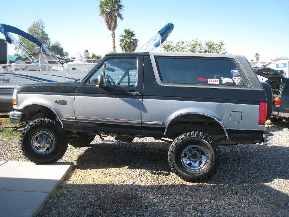 Two-tone black and silver lifted Ford Bronco with aftermarket wheels, parked on gravel