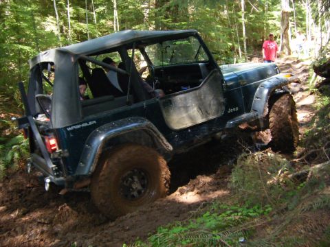 2005 Jeep Wrangler - Jeep Wrangler navigating a muddy trail through a forest, with people visible in the background.
