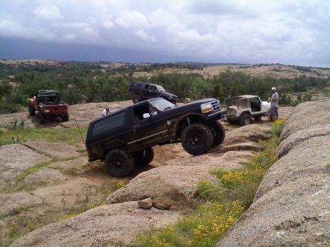 1995 Ford Bronco - Several off-road vehicles navigate a challenging rocky terrain under a cloudy sky.