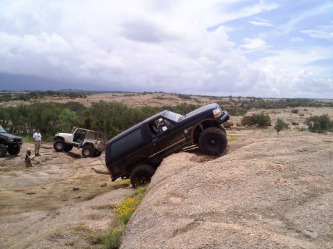 1995 Ford Bronco - A black 1995 Ford Bronco navigates a steep rocky incline, with other off-road vehicles and people observing the challenging terrain.