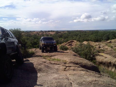 1995 Ford Bronco - Two off-road vehicles are parked on a rocky landscape under a cloudy sky.