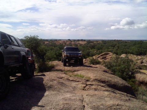 1995 Ford Bronco - Two off-road vehicles are parked on a rocky landscape under a cloudy sky.