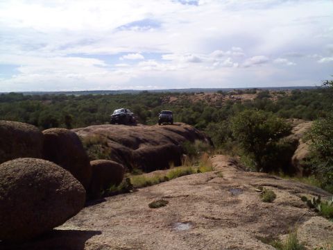 1995 Ford Bronco - Two SUVs are positioned on a rocky landscape with trees and hills in the background.