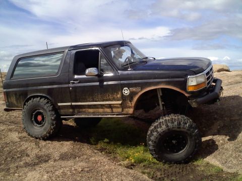 1995 Ford Bronco - A black Ford Bronco is shown off-road with a lifted suspension and large tires.