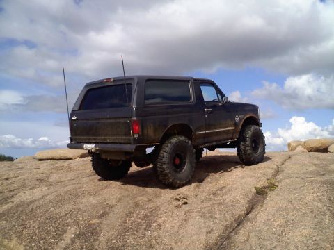 1995 Ford Bronco - This lifted 1995 Ford Bronco is shown off-road on a rocky landscape under a cloudy sky.