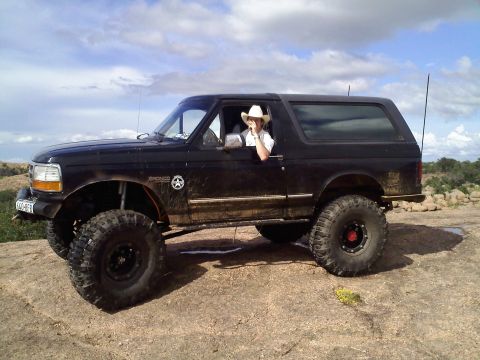 1995 Ford Bronco - Modified 1995 Ford Bronco off-roading on a rocky landscape with a person in a cowboy hat driving.