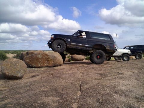 1995 Ford Bronco - A lifted 1995 Ford Bronco navigates a rocky terrain under a cloudy sky.
