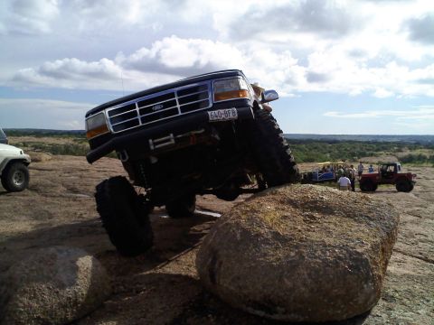 1995 Ford Bronco - A modified Ford Bronco navigates a rocky terrain with other vehicles in the background.