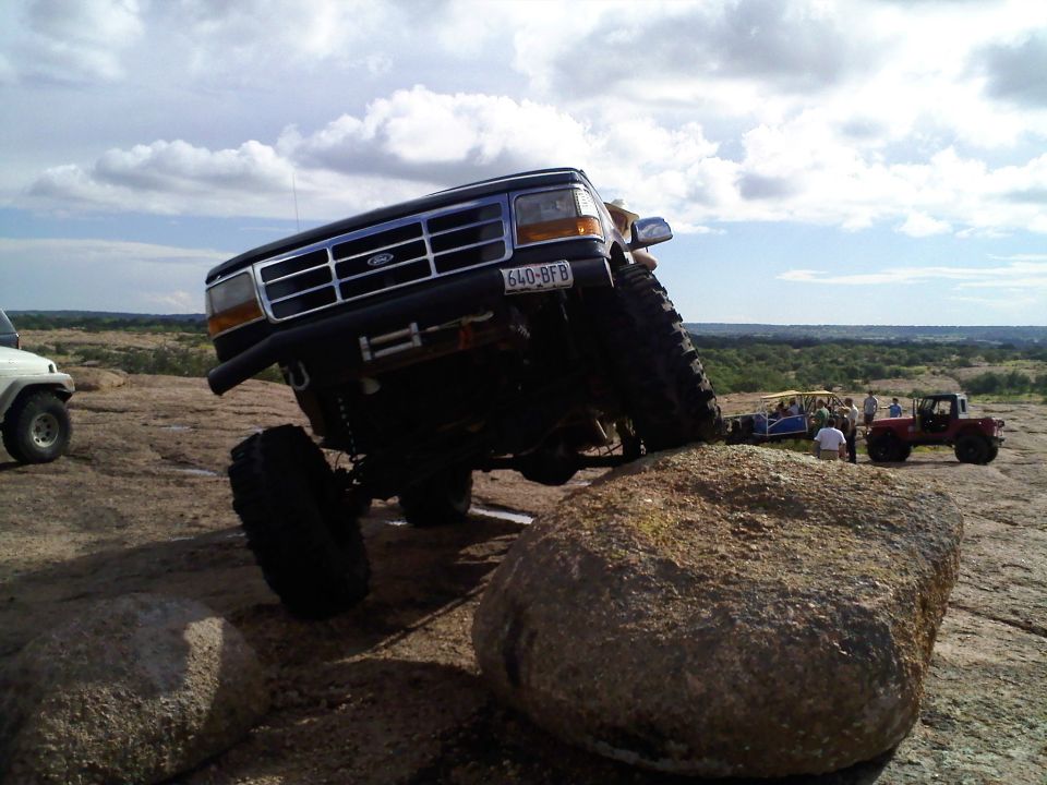 Dark blue Ford Bronco with large tires climbing over a rock, license plate 640-BFB