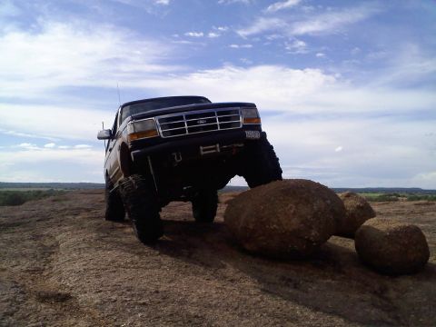 1995 Ford Bronco - A lifted Ford Bronco navigates rocky terrain under a cloudy sky.