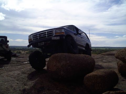 1995 Ford Bronco - This lifted 1995 Ford Bronco navigates rocky terrain under a cloudy sky.