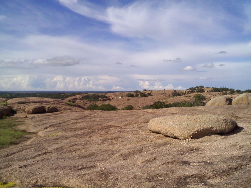wide shot of a rocky, arid landscape under a cloudy sky. A large, flat rock is in the foreground