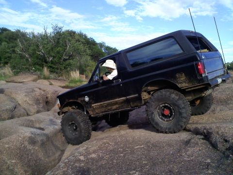 1995 Ford Bronco - A black Ford Bronco maneuvers over large rocks, demonstrating its off-road capabilities.