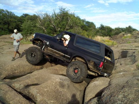 1995 Ford Bronco - A black 1995 Ford Bronco is shown off-roading over large rocks on a sunny day.
