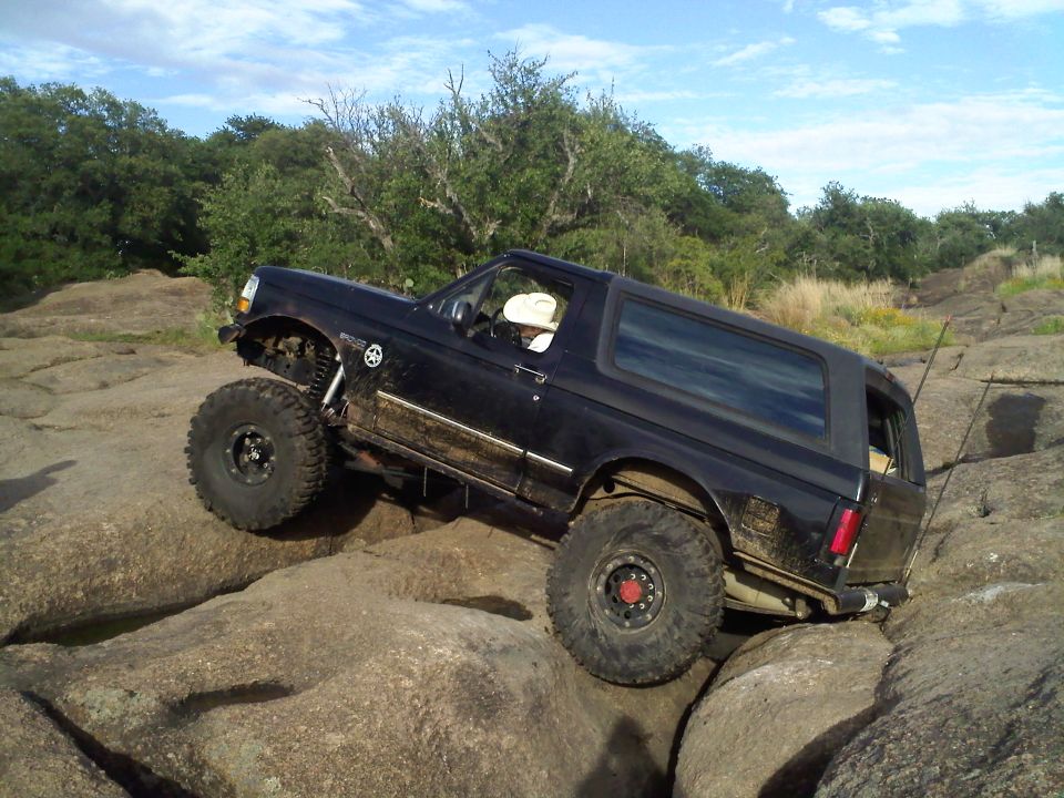 Black 1995 Ford Bronco climbing large rocks on an off-road trail