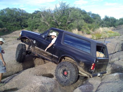 1995 Ford Bronco - A black SUV navigates a rocky terrain with a person in the driver's seat and another standing nearby.