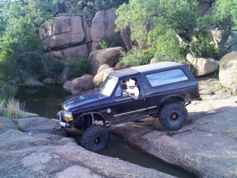 1995 Ford Bronco - A 1995 Ford Bronco drives through a rocky stream bed, demonstrating its off-road capabilities.