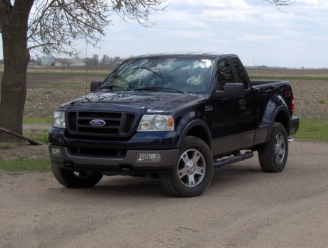 2005 Ford F-150 - A dark blue 2005 Ford F-150 pickup truck is parked on a dirt road with a field in the background.
