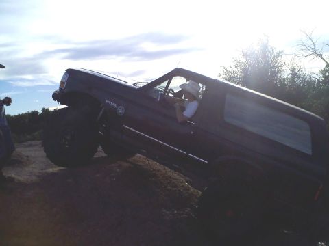 1995 Ford Bronco - A dark SUV, possibly a Ford Bronco, navigates an off-road trail with a driver wearing a cowboy hat.