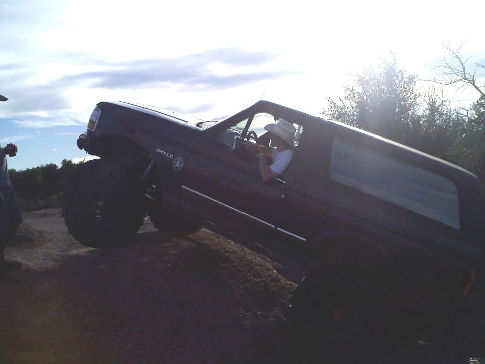 Dark SUV with lifted suspension and large tires, angled on a dirt incline. A person in a cowboy hat is driving