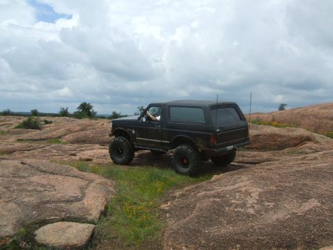 1995 Ford Bronco - A black 1995 Ford Bronco navigates a rocky landscape with a driver visible inside.