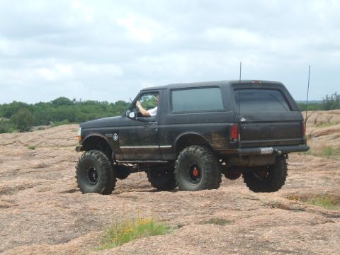 1995 Ford Bronco - A black Ford Bronco navigates a , rocky landscape under a cloudy sky.