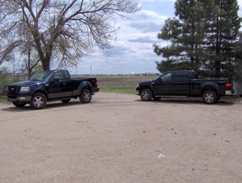 2005 Ford F-150 - Two Ford F-150 trucks, a regular cab and a crew cab, are parked side-by-side in a dirt lot.