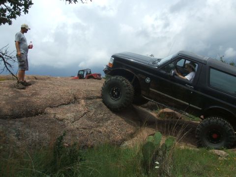 1995 Ford Bronco - A black 1995 Ford Bronco navigates a challenging rocky terrain, with another off-road vehicle visible in the distance.