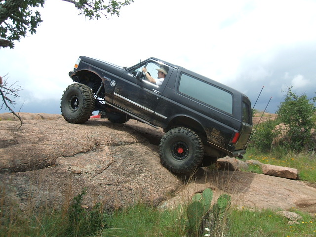 1995 Ford Bronco climbing large rocks off-road. Driver wears a hat