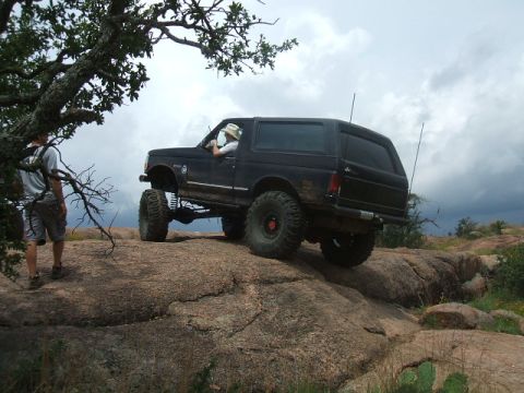 1995 Ford Bronco - A black Ford Bronco navigates a rocky terrain under a cloudy sky.