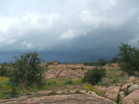 1995 Ford Bronco - A dramatic sky looms over a terrain dotted with vegetation and large rocks, suggesting an approaching storm.