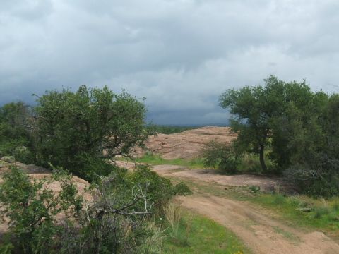 1995 Ford Bronco - A dirt road passes through a rocky, tree-filled landscape with a cloudy sky overhead.