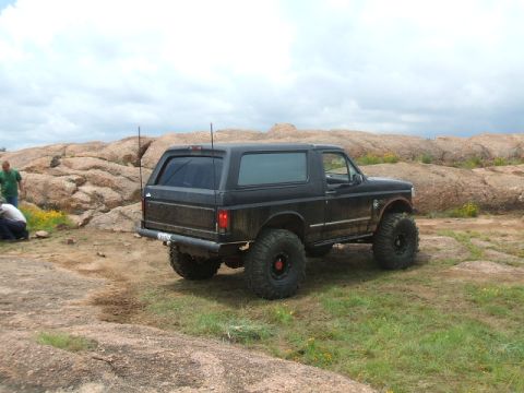 1995 Ford Bronco - A black SUV is parked on a rocky hill with two people nearby.