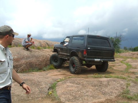 1995 Ford Bronco - A black Ford Bronco navigates a challenging rocky landscape under a cloudy sky.