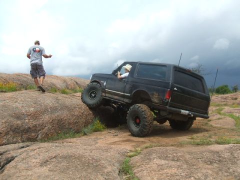 1995 Ford Bronco - A black 1995 Ford Bronco navigates a rocky off-road course with a person watching.
