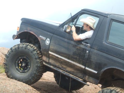 1995 Ford Bronco - A black 1995 Ford Bronco navigates a rocky trail, its driver visible behind the wheel.