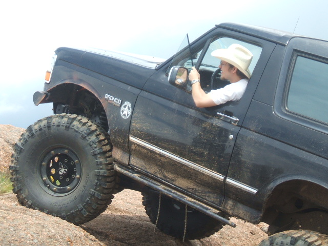 Black 1995 Ford Bronco with large tires on rocky terrain, driver wearing a cowboy hat