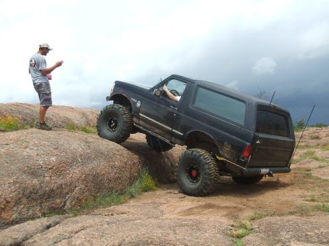 1995 Ford Bronco - A lifted black 1995 Ford Bronco navigates a rocky terrain, demonstrating its off-road capabilities.
