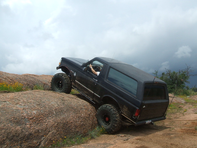 Black SUV climbing over large rocks with a person driving