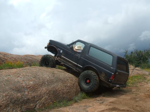 1995 Ford Bronco - A black 1995 Ford Bronco navigates a challenging rocky terrain, its large tires gripping the uneven surface.