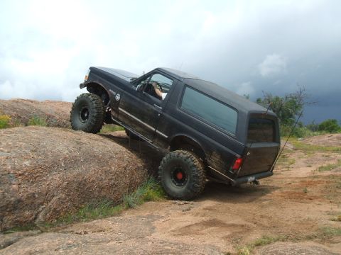 1995 Ford Bronco - A black 1995 Ford Bronco navigates a challenging rocky terrain under a cloudy sky.