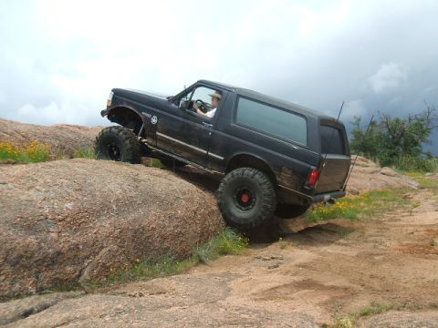 1995 Ford Bronco - A black Ford Bronco navigates a challenging rocky terrain with its tires gripping the stones.