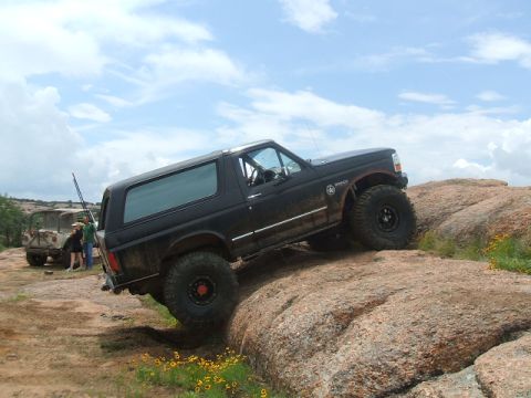 1995 Ford Bronco - A black 1995 Ford Bronco navigates a challenging rocky terrain, with another vehicle visible in the distance.
