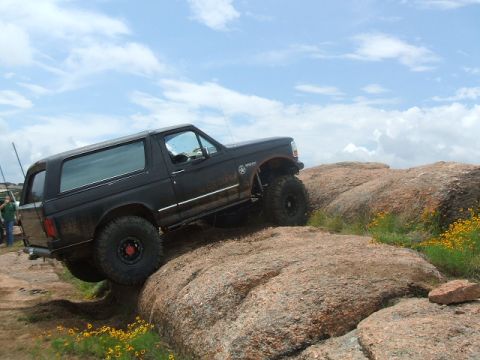 1995 Ford Bronco - A black Ford Bronco navigates a rocky off-road course under a cloudy sky.