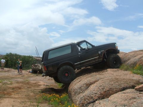 1995 Ford Bronco - A black 1995 Ford Bronco navigates a challenging rocky terrain under a cloudy sky.