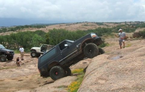 1995 Ford Bronco - A black Ford Bronco navigates a steep, rocky terrain with other vehicles and onlookers present.