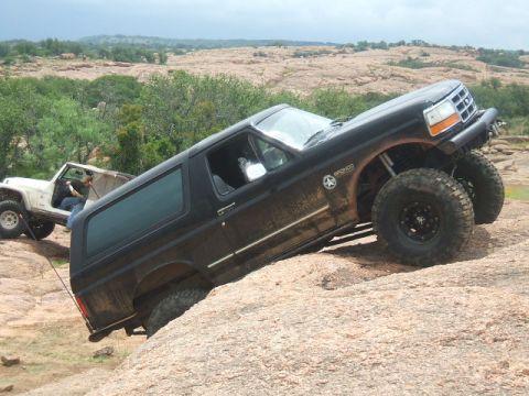 1995 Ford Bronco - A black 1995 Ford Bronco navigates a steep, rocky incline with a white Jeep in the background.